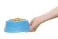 Female hand holding blue plastic feeding bowl filled with cat kibble isolated on a white background