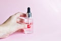 Female hand holding bottle of moisturizing face oil on a pink background. A professional product for a perfect complexion. Women`s Royalty Free Stock Photo