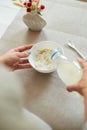 Female hand holding bottle pouring milk in cereal granola flakes bowl Royalty Free Stock Photo