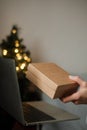 Female hand holding a brown box over the keyboard a laptop. Christmas shopping online at home Royalty Free Stock Photo