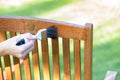 female hand holding a brush applying varnish paint on a wooden garden chair - painting and caring for wood