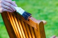 female hand holding a brush applying varnish paint on a wooden garden chair- painting and caring for wood