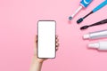 Female hand holding cellphone and various toothbrushes, toothpaste and mouth freshener, on a pink background. Mock up. The concept