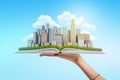 Female hand holding city skyscrapers on an open book on blue background