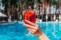 Female hand holding cocktail. Swimming pool on the background. Cropped, copy space. Summer, party, vacation and Royalty Free Stock Photo