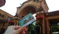 Female hand holding a Copenhagen card on the background of the entrance to Tivoli Park in Copenhagen. A tourist card