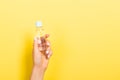 Female hand holding cream bottle of lotion isolated. Girl give jar cosmetic products on yellow background Royalty Free Stock Photo