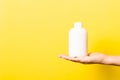 Female hand holding cream bottle of lotion isolated. Girl give tube cosmetic products on yellow background Royalty Free Stock Photo