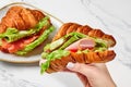 Female hand holding croissant with fried egg, ham, salami, cheese, tomatoes and lettuce Royalty Free Stock Photo