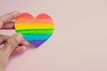 Female hand holding decorative Heart with rainbow stripes on pink background. LGBT pride flag, symbol of lesbian, gay, bisexual, Royalty Free Stock Photo