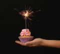 Female hand holding delicious birthday cupcake with firework candle on dark background Royalty Free Stock Photo