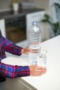 Female hand holding drinking water bottle and pouring water into glass on table on blurred kitchen background. Royalty Free Stock Photo