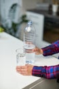 Female hand holding drinking water bottle and pouring water into glass on table on blurred kitchen background. Royalty Free Stock Photo