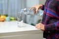 Female hand holding drinking water bottle and pouring water into glass on table on kitchen background. Royalty Free Stock Photo