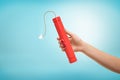 A female hand holding a dynamite stick with a burning wick on blue background.