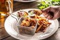 Female hand holding a fried chicken nugget dipped in a white sauce over a plate with french fries, and salad Royalty Free Stock Photo