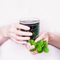 Female hand holding glass of green chlorophyll drink with mint leaves on a light pink background