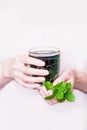 Female hand holding glass of green chlorophyll drink with mint leaves on a light pink background. Copy space
