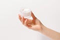 Female hand holding glass jar of face cream on white isolated background. The concept of moisturizing and nourishing the skin,