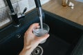 Human hand holding glass pouring fresh drink water at kitchen faucet Royalty Free Stock Photo