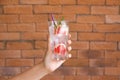 Female hand holding glass of refreshing grapefruit lemonade against brick wall