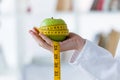 Female hand holding a green apple wrapped in a tape measure.