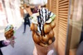 Female hand holding an ice cream cone with waffles, fruits and chocolate against a blurred background of a busy street. Selective Royalty Free Stock Photo