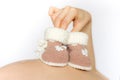 Female hand holding knitted booties for newborn babies on background of the pregnant belly