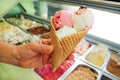 Female hand is holding a large strawberry, mint, vanilla with sour cherry ice cream in waffle cone.