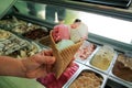 Female hand is holding a large strawberry, mint, vanilla with sour cherry ice cream in waffle cone.