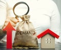 A female hand is holding a magnifying glass over a money bag with the word Demand, up arrow and a house. The concept of high Royalty Free Stock Photo