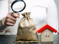 A female hand is holding a magnifying glass over a money bag with the word Mortgage and a wooden house. Concept analysis of Royalty Free Stock Photo