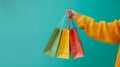 Person holding multiple vibrant shopping bags against a bright teal backdrop with copy space Royalty Free Stock Photo