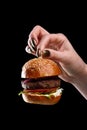 Female hand holding mini burger as a Christmas tree toy on black background Royalty Free Stock Photo