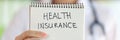 Female hand holding notepad with health insurance lettering Royalty Free Stock Photo