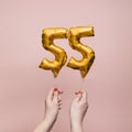 Female hand holding a number 55 birthday anniversary celebration gold balloon