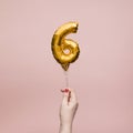 Female hand holding a number 6 birthday anniversary celebration gold balloon