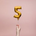 Female hand holding a number 5 birthday anniversary celebration gold balloon
