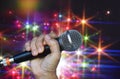 A female hand is holding one microphone against the colorful lights Royalty Free Stock Photo