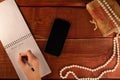 Female hand holding pen on open notepad. Woman writes goals for new year 2020. Smartphone and pearl necklace on wooden table. Conc