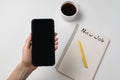 Female hand holding phone. Notepad, pen and cup of coffee on white background. New job. Copy space Royalty Free Stock Photo