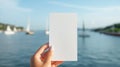 Female hand holding a piece of white paper on a blurred background of an ocean bay with yachts.