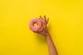 Female hand holding pink donut over yellow background. Top view, flat lay. Sweet, dessert, diet concept. Banner with copy space. Royalty Free Stock Photo