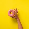 Female hand holding pink donut over yellow background. Top view, flat lay. Sweet, dessert, diet concept. Banner with copy space. Royalty Free Stock Photo