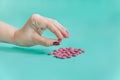 Female hand holding  pink pills. Turquoise background. Close-up view Royalty Free Stock Photo