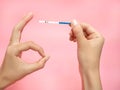 Female hand holding positive pregnancy test and Showing gesture OK isolated on pink background. The abbreviation HCG on