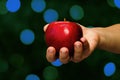 Female hand holding red apple on defocused abstract blue bokeh lights dark background. Close-up. Copy space Royalty Free Stock Photo