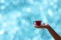 Female hand holding a red cup of coffee with blurred blue bokeh background Royalty Free Stock Photo