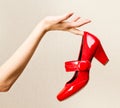 Female hand holding red varnish shoes on a high heel.