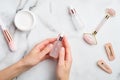 Female hand holding serum bottle over marble table with moisturizer cream, makeup brush, face massage roller. Flat lay, top view. Royalty Free Stock Photo